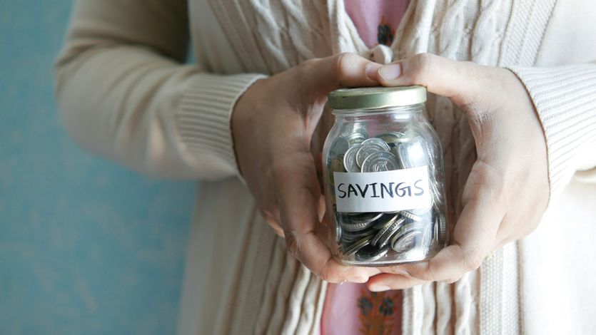 A woman holds a jar of coins marked savings.