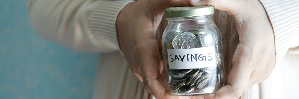 A woman holds a jar of coins marked savings.