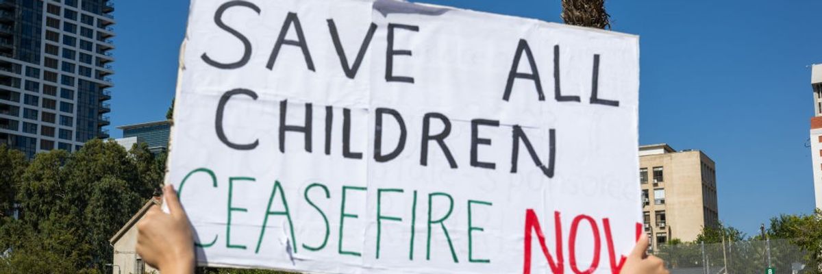 A woman holds a "Save all children, ceasefire now" sign