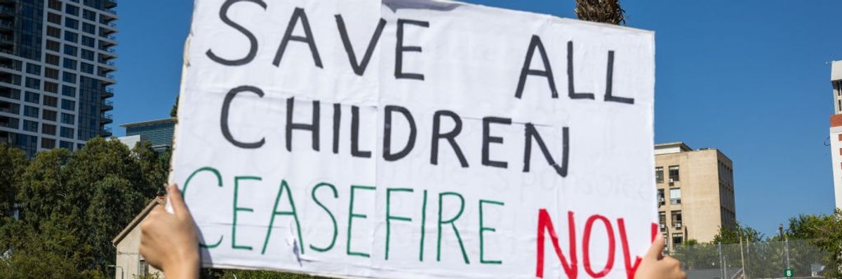 A woman holds a "Save all children, ceasefire now" sign