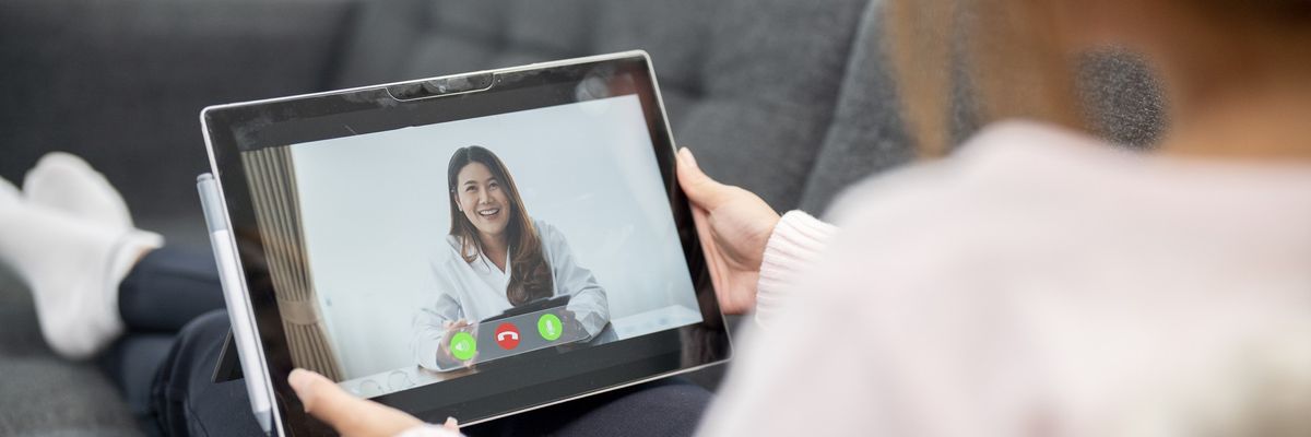A woman holds a tablet while attending a telemedicine appointment.
