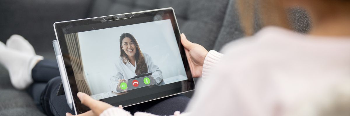 A woman holds a tablet while attending a telemedicine appointment. 