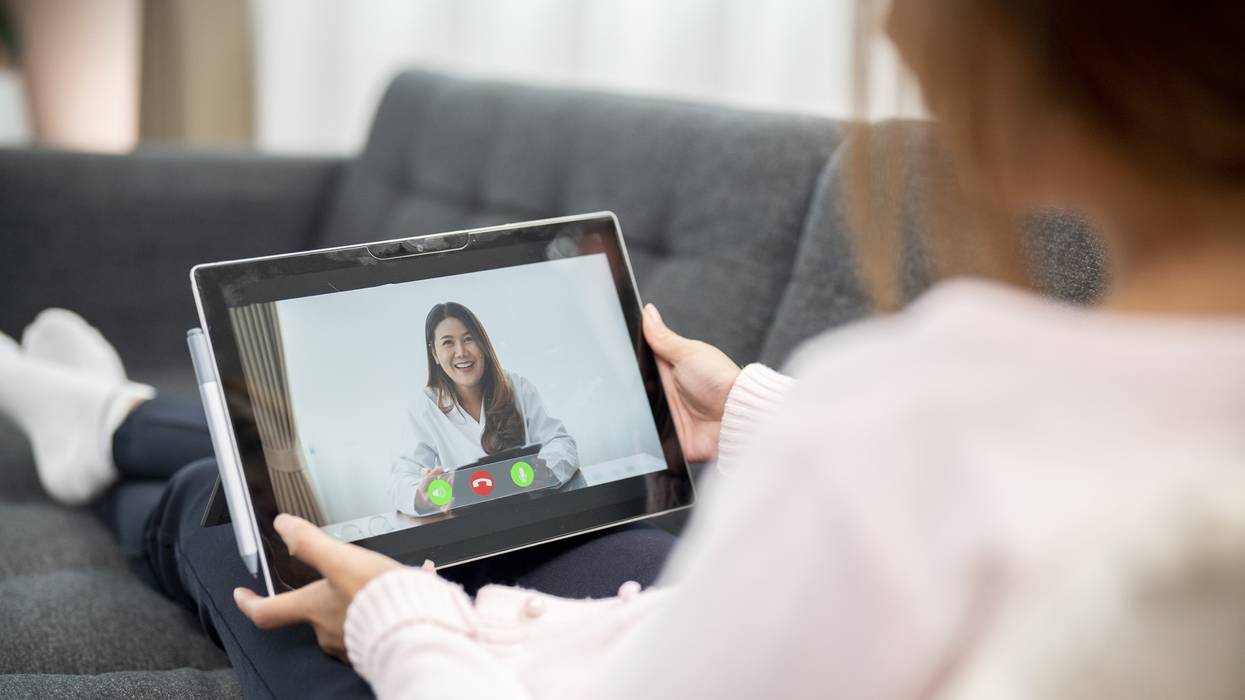 A woman holds a tablet while attending a telemedicine appointment.