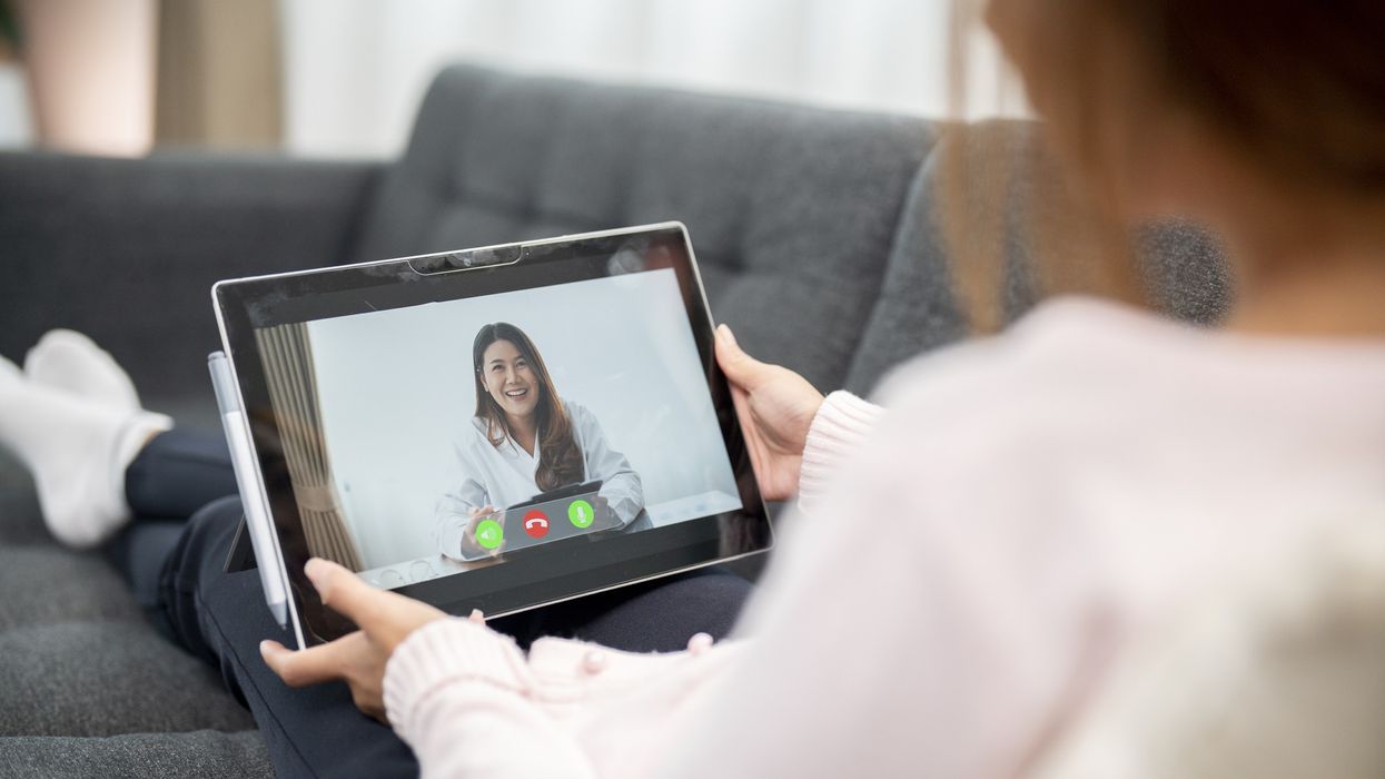 A woman holds a tablet while attending a telemedicine appointment.