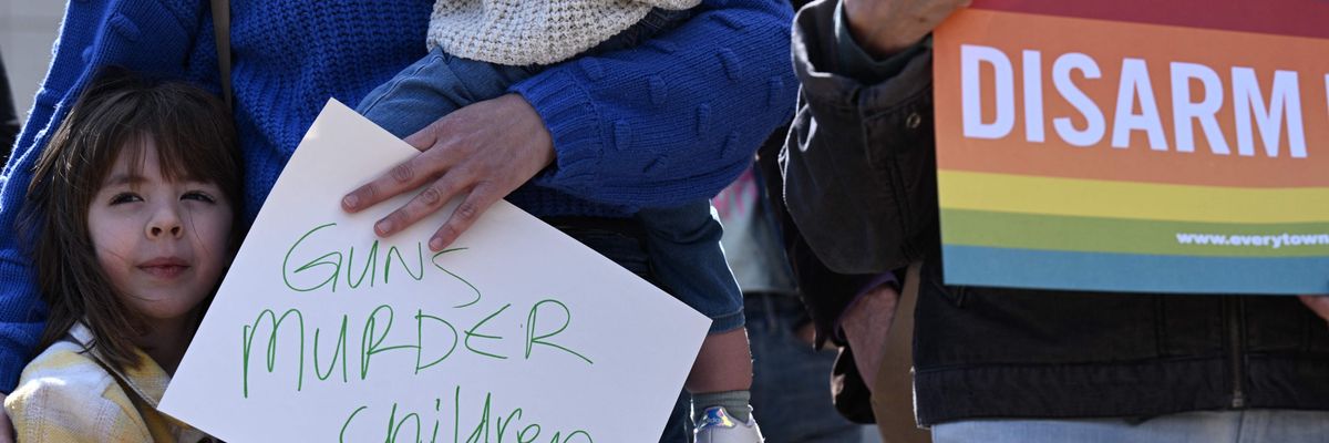 A woman holds her two children and a sign reading "Guns Murder Children"