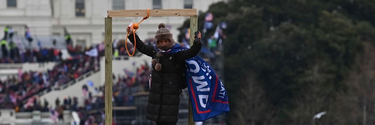 A woman holds up a noose and wears a Trump flag as a cape. 