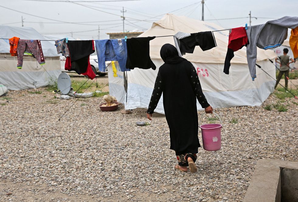 A woman in a black dress carries a pink water bucket.