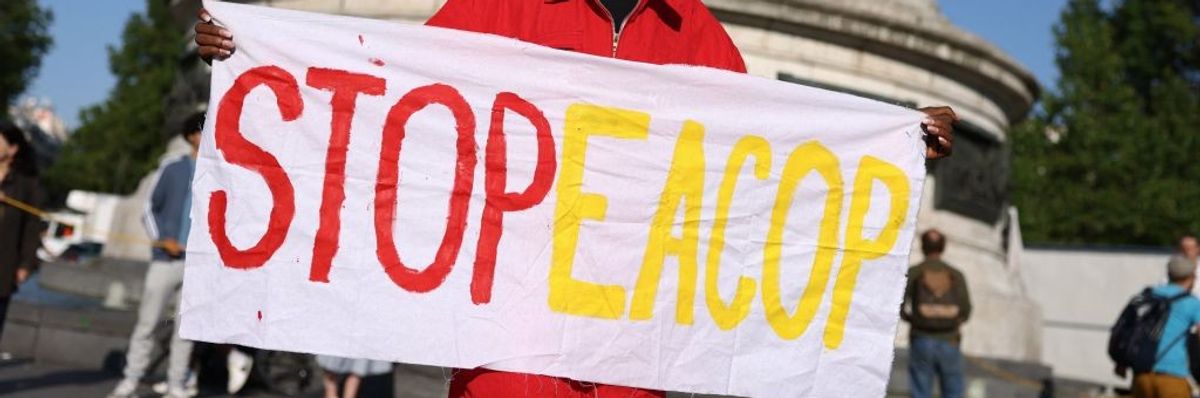 A woman in a red coat holds a sign saying, "Stop EACOP."