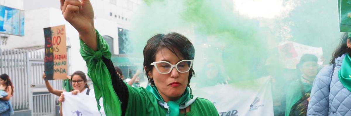 A woman in green raises a green smoke flare into the air.