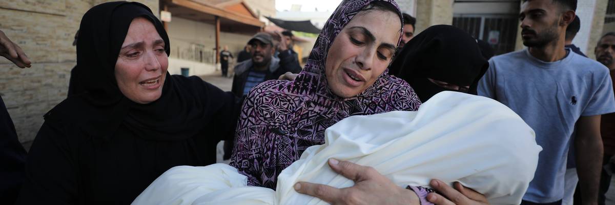 A woman mourns as she carries the body of a child killed in Israeli attacks
