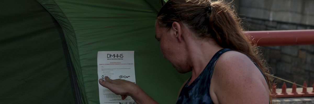 A woman points to a note on her tent alerting her of a scheduled encampment cleanup