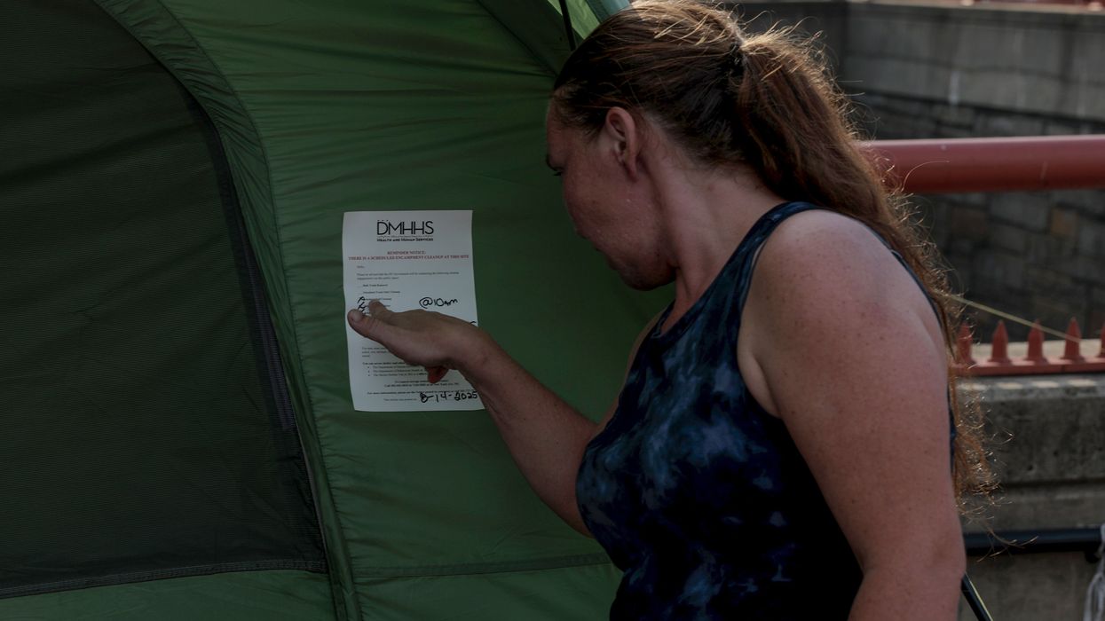 A woman points to a note on her tent alerting her of a scheduled encampment cleanup
