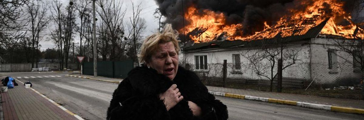 A woman reacts as she stands in front of a house burning after being shelled in the city of Irpin