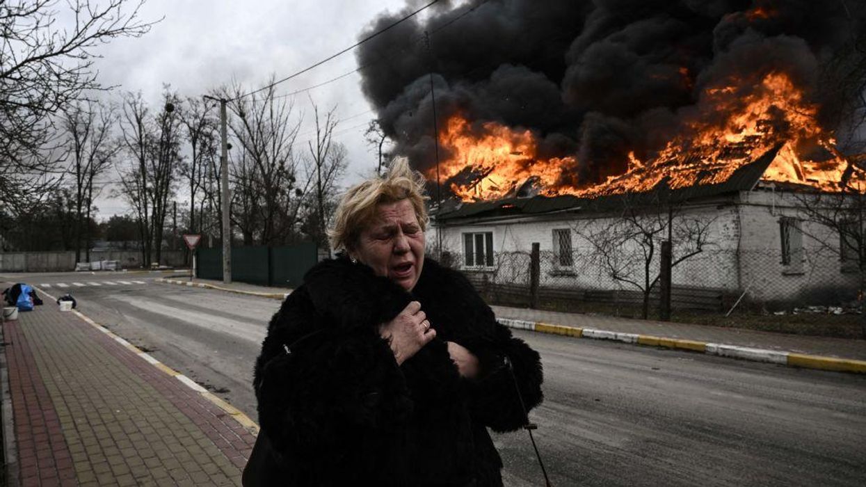 A woman reacts as she stands in front of a house burning after being shelled in the city of Irpin