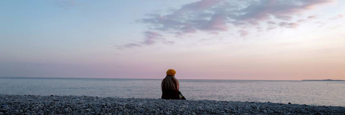 A woman sits and looks at the ocean.