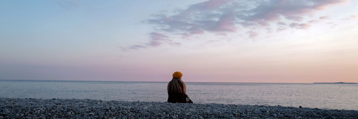 A woman sits and looks at the ocean.