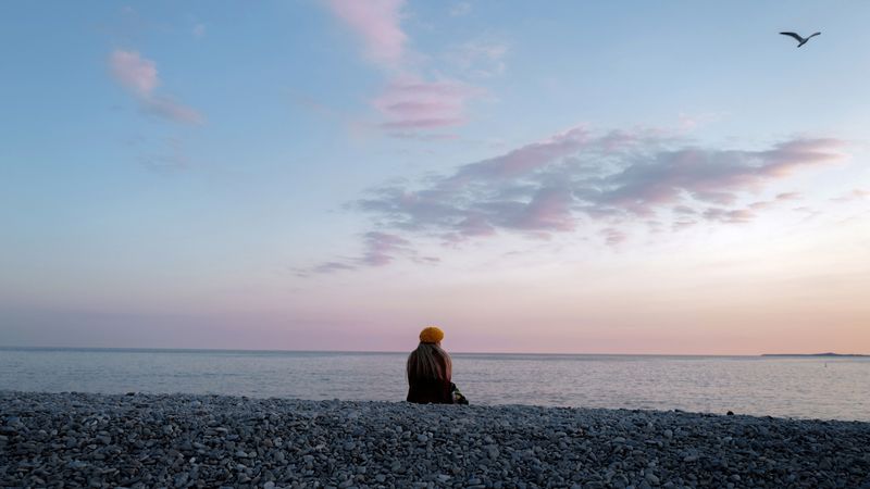 A woman sits and looks at the ocean.