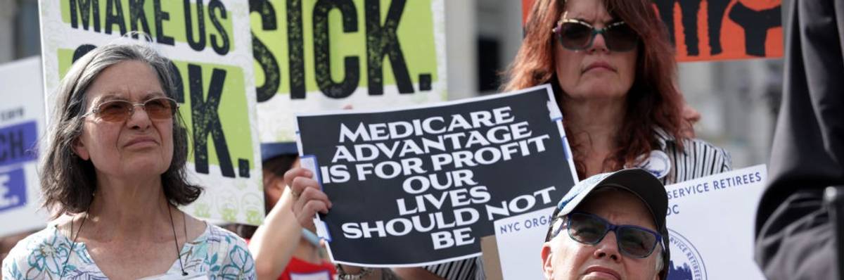 A woman stands at a rally with a sign reading, "Medicare Advantage is for profit our lives should not be."