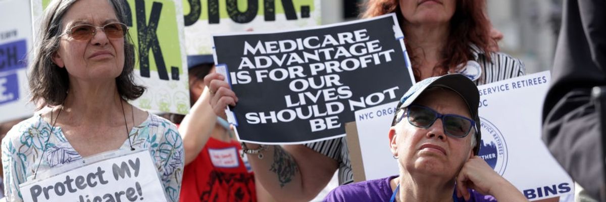 A woman stands at a rally with a sign reading, "Medicare Advantage is for profit our lives should not be."
