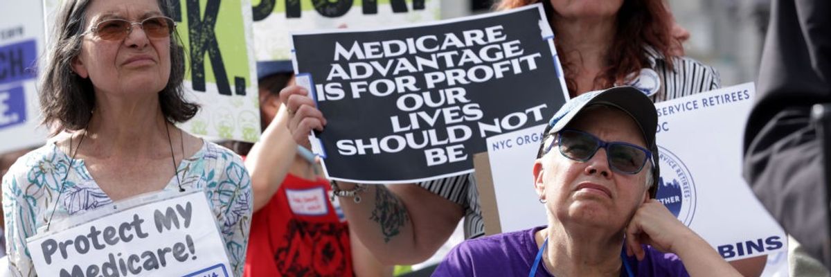 A woman stands at a rally with a sign reading, "Medicare Advantage is for profit our lives should not be."