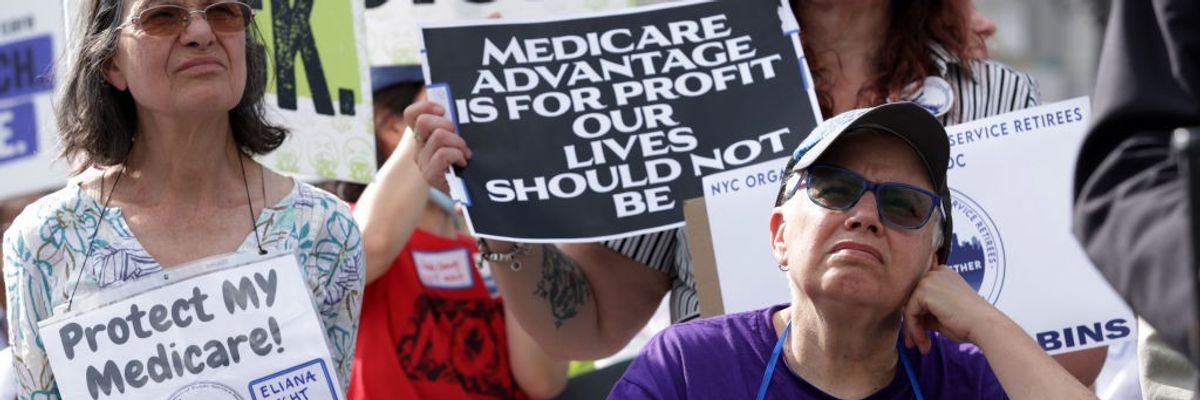 A woman stands at a rally with a sign reading, "Medicare Advantage is for profit our lives should not be."