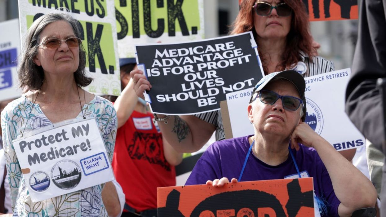 A woman stands at a rally with a sign reading, "Medicare Advantage is for profit our lives should not be."