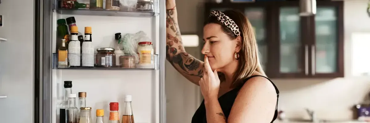 A woman stands in front of a refrigerator.