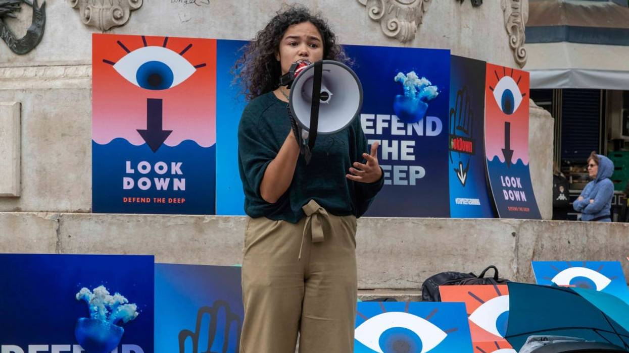 A woman stands with a megaphone in front of posters saying, "Look Down," and "Defend the Deep."
