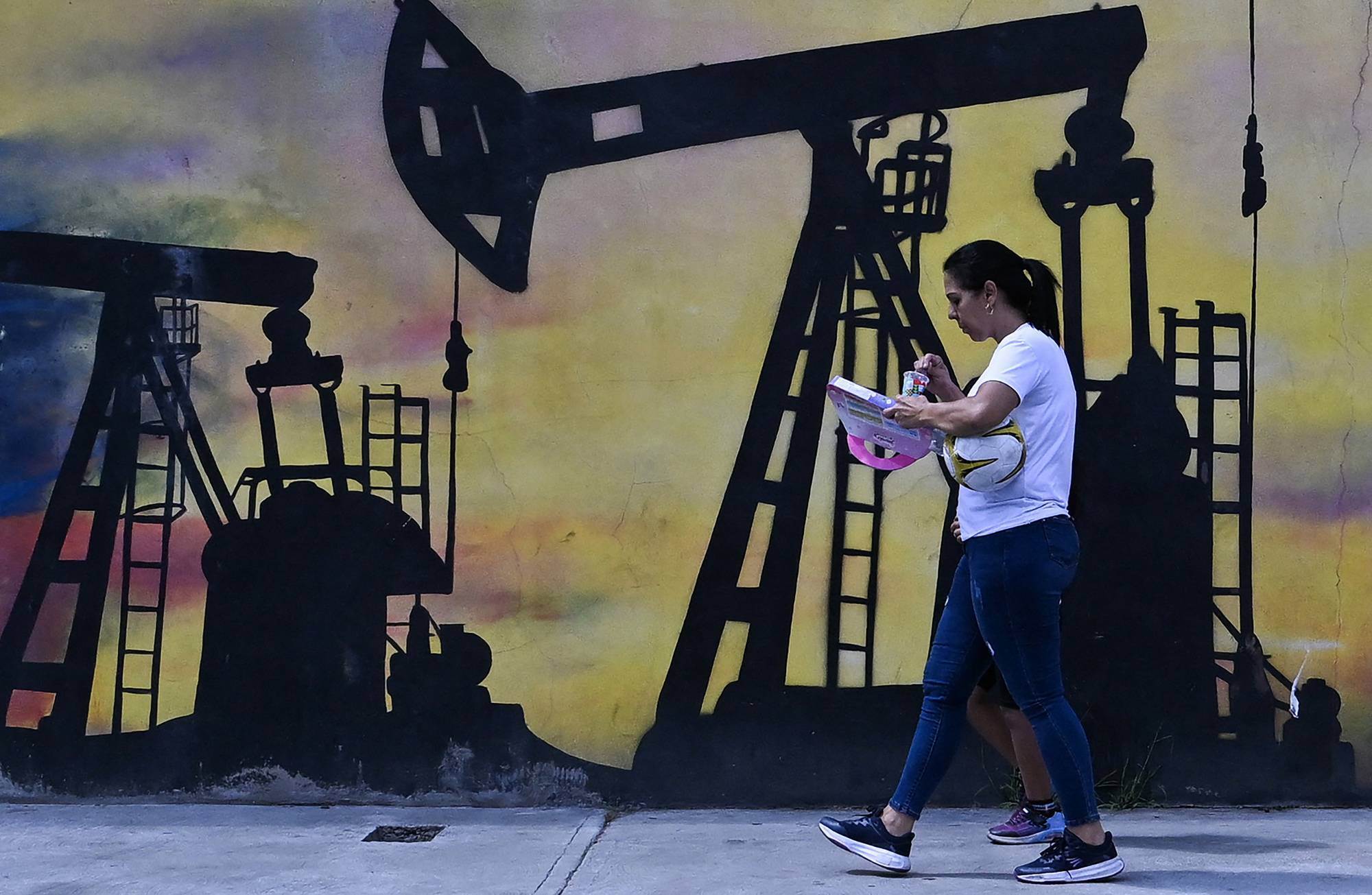 A woman walks past a mural of an oil pump in Venezuela.