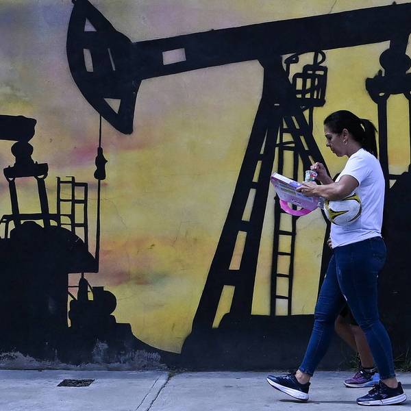 A woman walks past a mural of an oil pump in Venezuela.