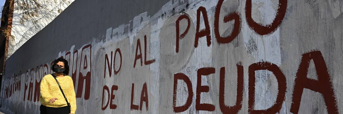 A woman walks past a wall reading, "No to debt payment" in Spanish.