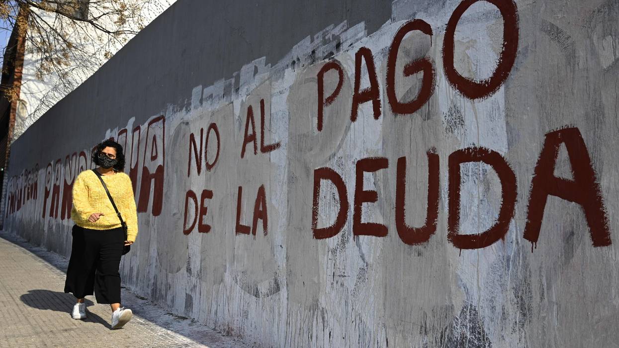 A woman walks past a wall reading, "No to debt payment" in Spanish.