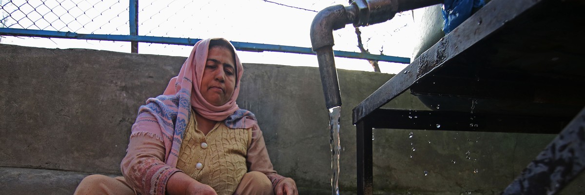 A woman washes dishes at a water supply station in Kashmir, India on March 22, 2023.