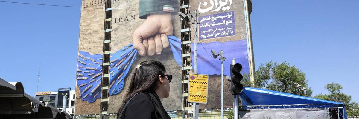 A woman without a head covering walks by a mural depicting an Iranian hand squeezing closed the Strait of Hormuz