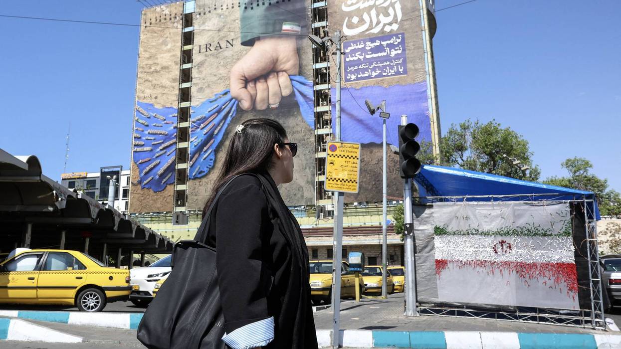 A woman without a head covering walks by a mural depicting an Iranian hand squeezing closed the Strait of Hormuz