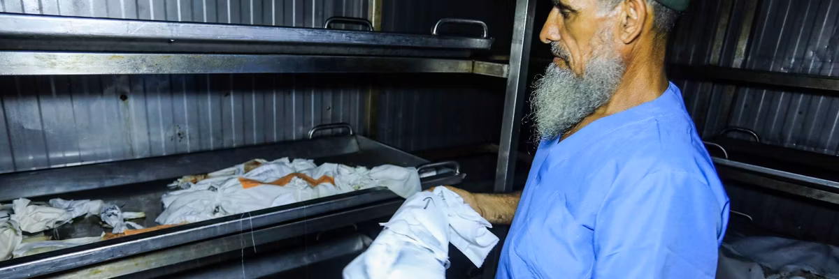 A worker at Nasser Hospital's morgue adds the wrapped body of a dead newborn to a tray containing 19 others