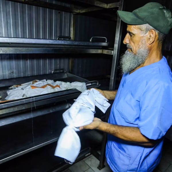 A worker at Nasser Hospital's morgue adds the wrapped body of a dead newborn to a tray containing 19 others