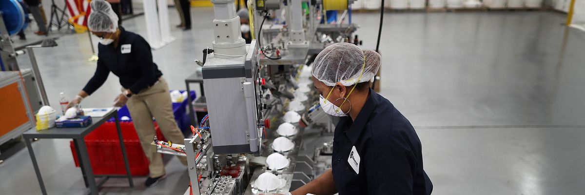 A worker gathers N95 masks off an assembly line