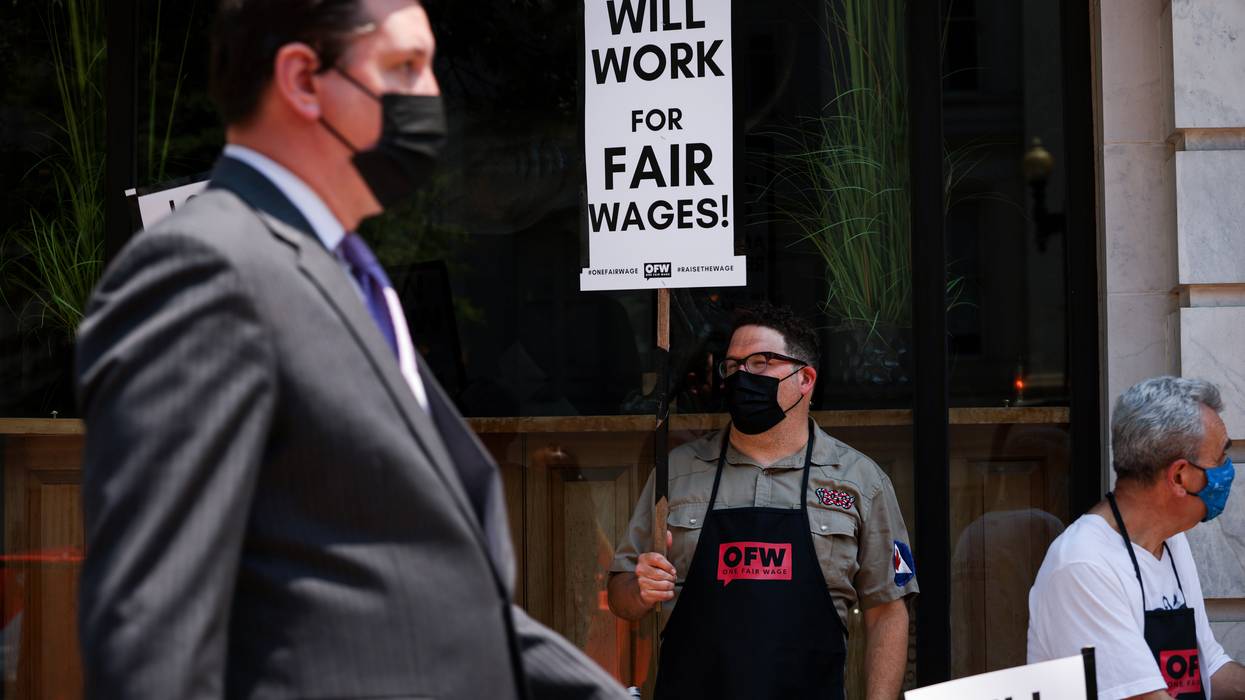 A worker holds a sign reading, "Will work for fair wages!"