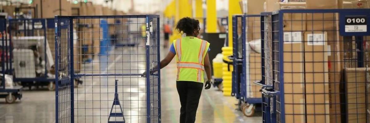 A worker pulls a blue cart through an Amazon warehouse.