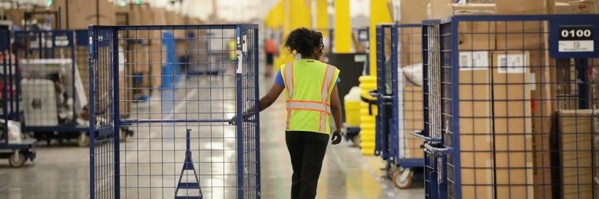 A worker pulls a blue cart through an Amazon warehouse. 