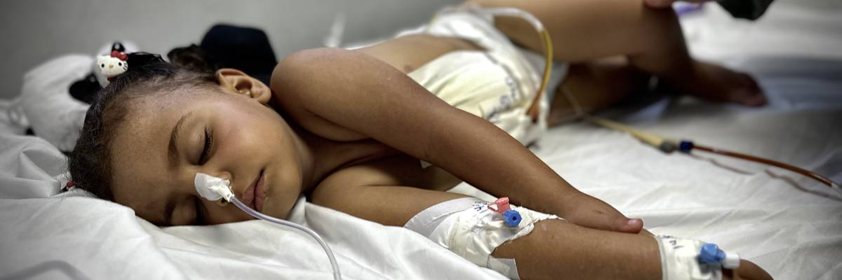 A wounded 2 year old lies on a bed in Gaza.