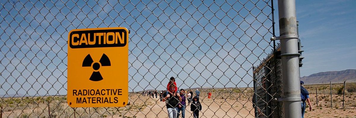 A yellow sign saying, "Caution: Radioactive Materials" is attached to a chain-linked fence at the Trinity Site.