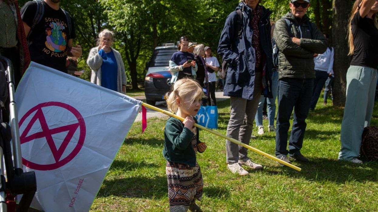 A young child standing on grass holds a red and white Extinction Rebellion flag.