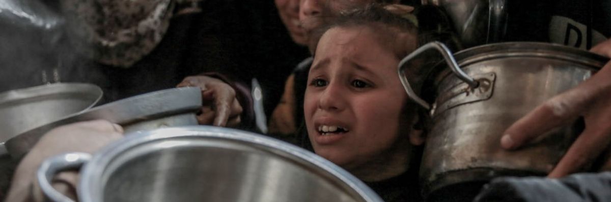 A young girl among a crowd of hungry Gazans holding pots at a charity food distribution center