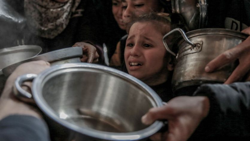 A young girl among a crowd of hungry Gazans holding pots at a charity food distribution center