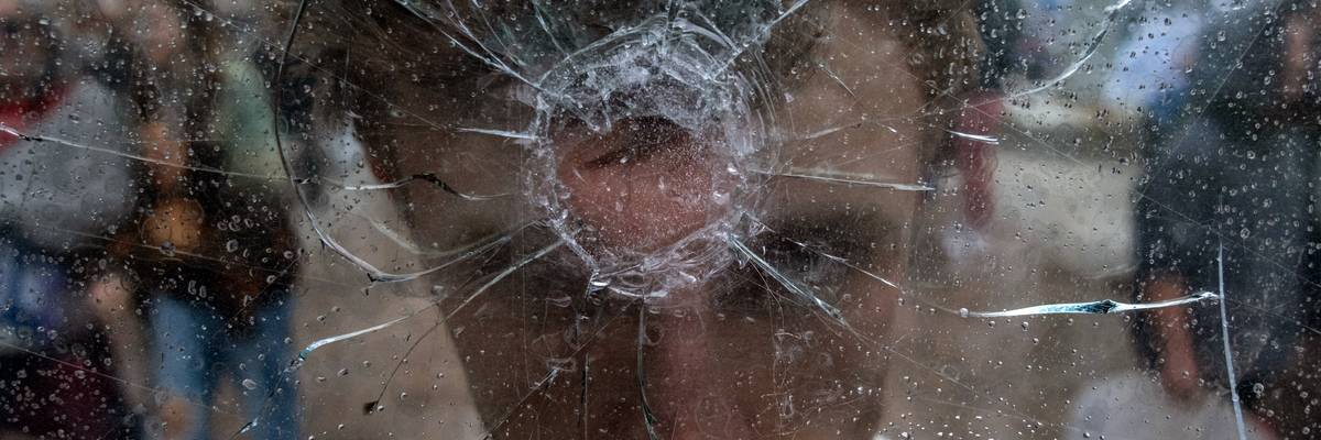 A young protester marching for gun reform holds up a window shattered by a bullet.