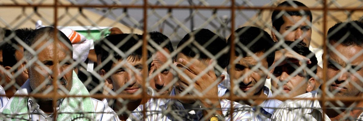 Abu Ghraib detainees behind chain-linked fence.