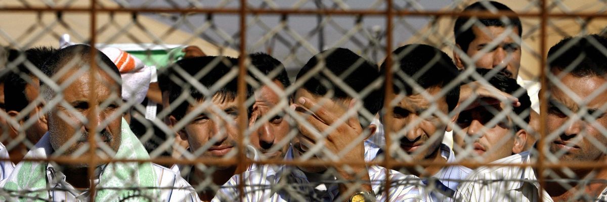Abu Ghraib detainees behind chain-linked fence. 