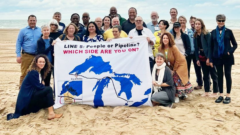 Activists gather around a sign reading, "Line 5: people or pipeline? Which side are you on?"